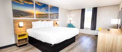 A hotel room with a large bed, wooden floor, a desk, and a view of the outdoors.