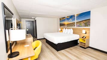 A hotel room with a bed, a desk with a chair, a nightstand, and a wall-mounted lamp.