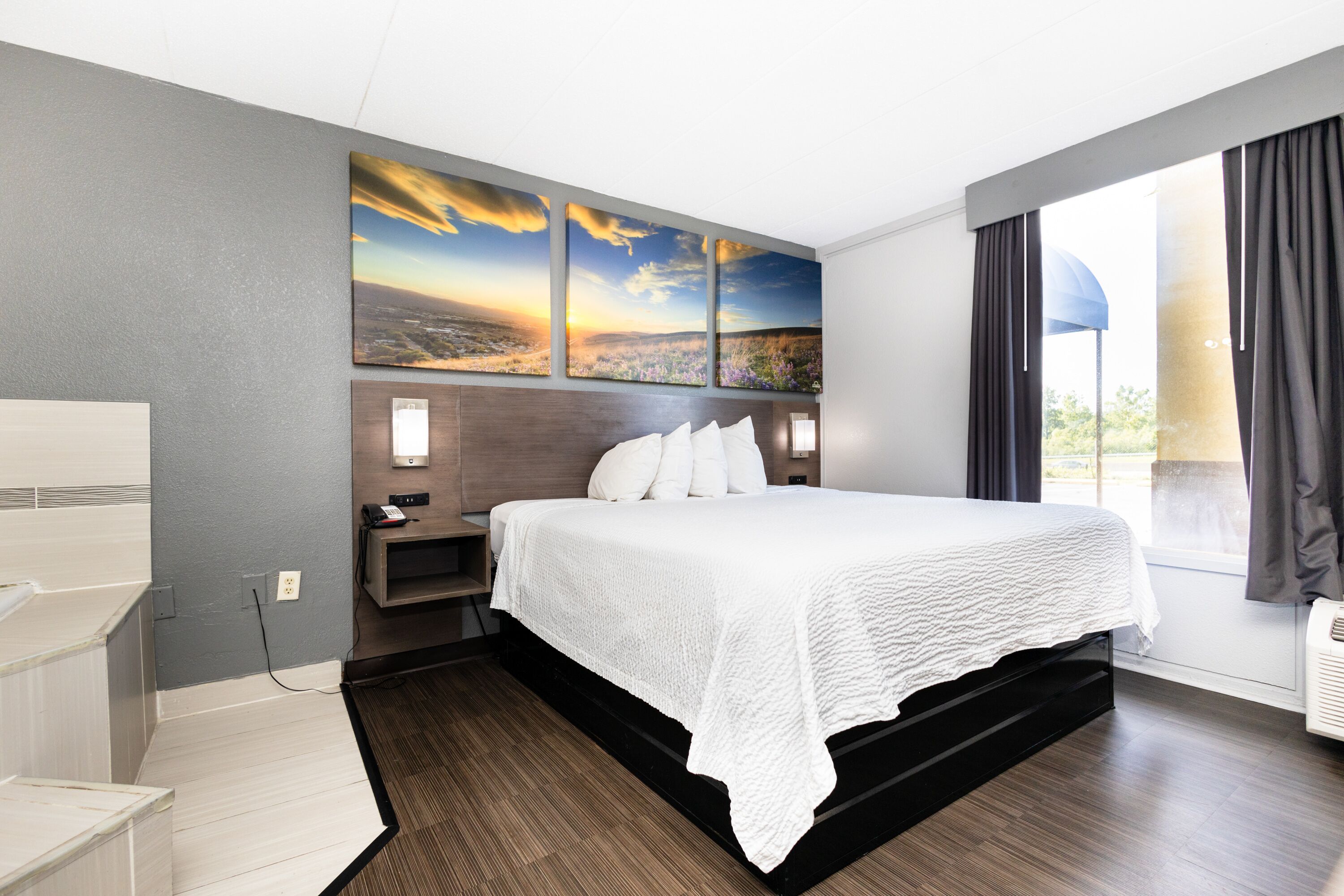 Habitació d'hotel amb un llit gran, una tauleta de nit, un escriptori i una finestra amb cortines.