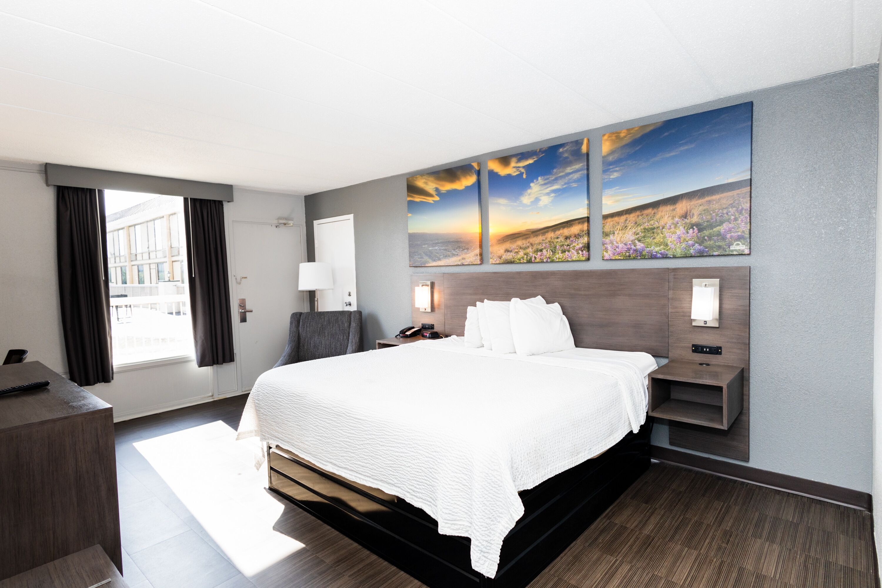 Ein modernes Hotelzimmer mit einem großen Bett, einem Schreibtisch, einem Stuhl und Blick auf ein Feld.