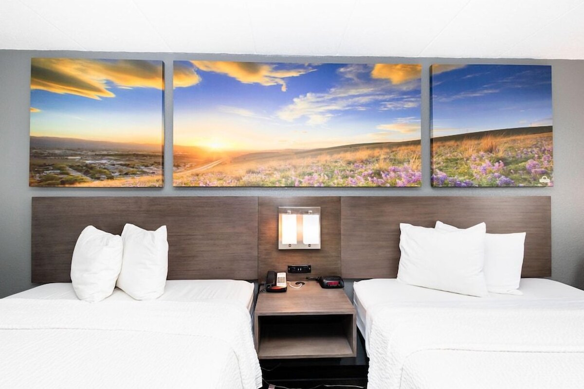 Quarto de hotel com duas camas, mesa de cabeceira, telefone e luminária fixada na parede.