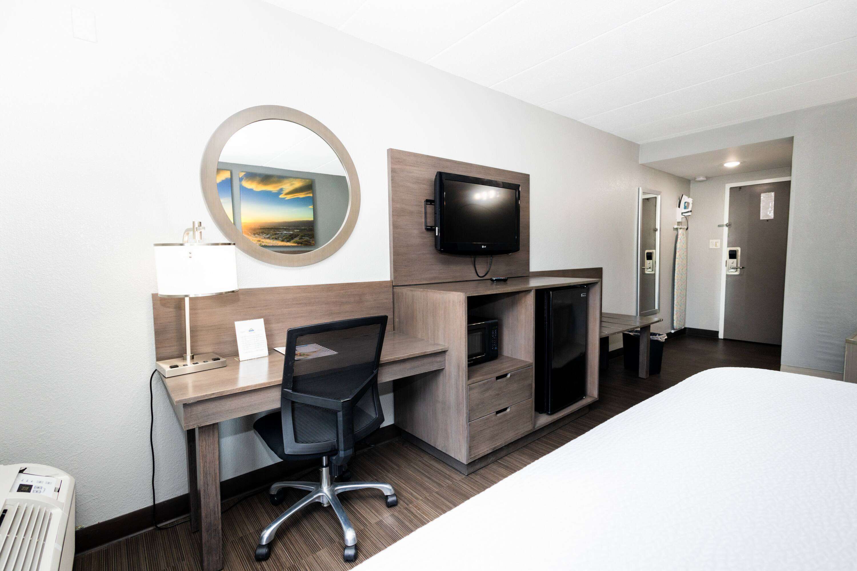 Una habitación de hotel con cama, escritorio, silla, televisión y espejo.