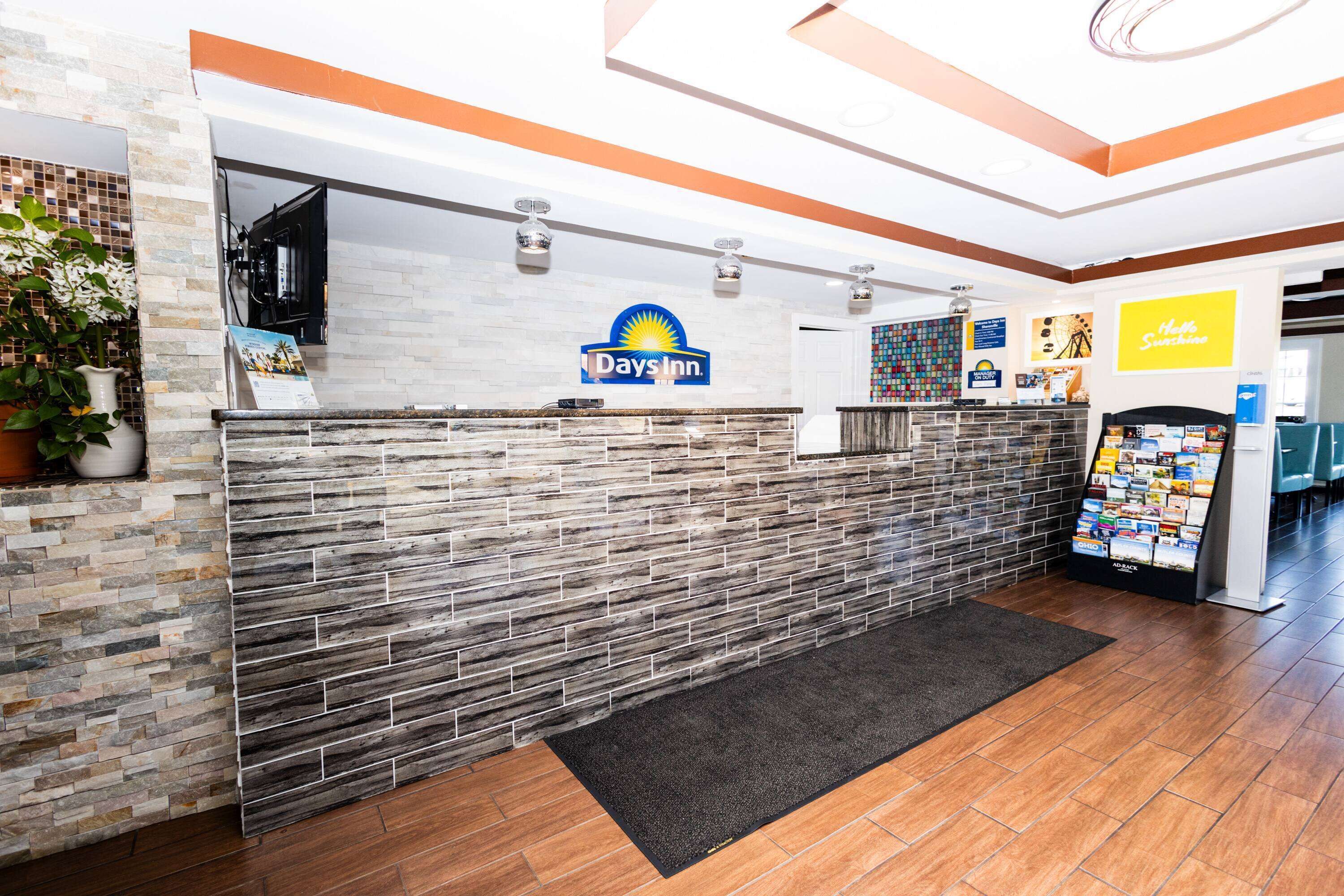 A reception area with a Days Inn sign, a reception desk, a plant, and a bulletin board.