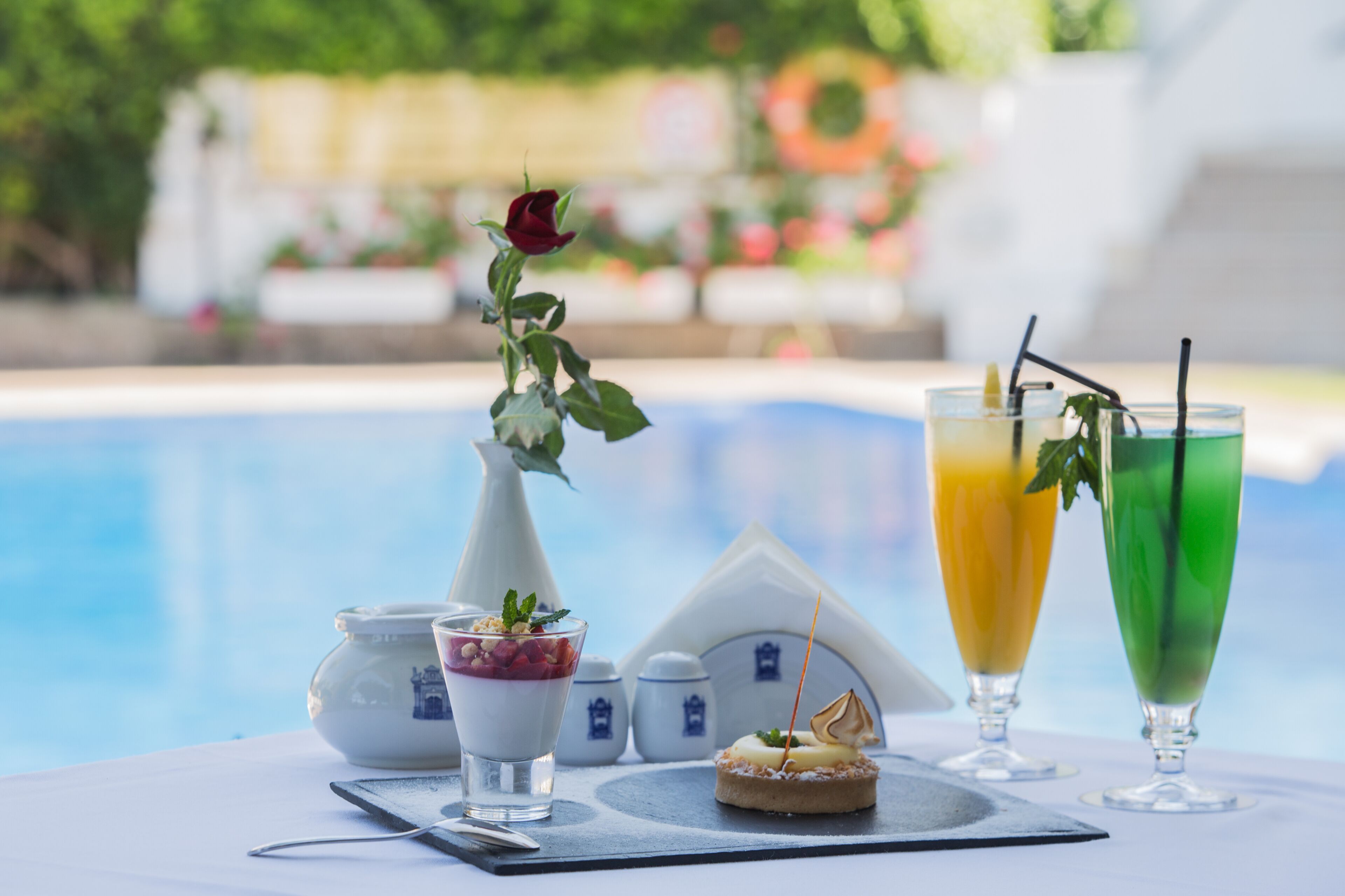 Une table avec un dessert, un vase contenant une rose et deux boissons servies avec des pailles.