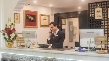 Un mostrador de recepción de hotel con un hombre hablando por teléfono, premios enmarcados en la pared y un letrero que indica la zona de recepción.