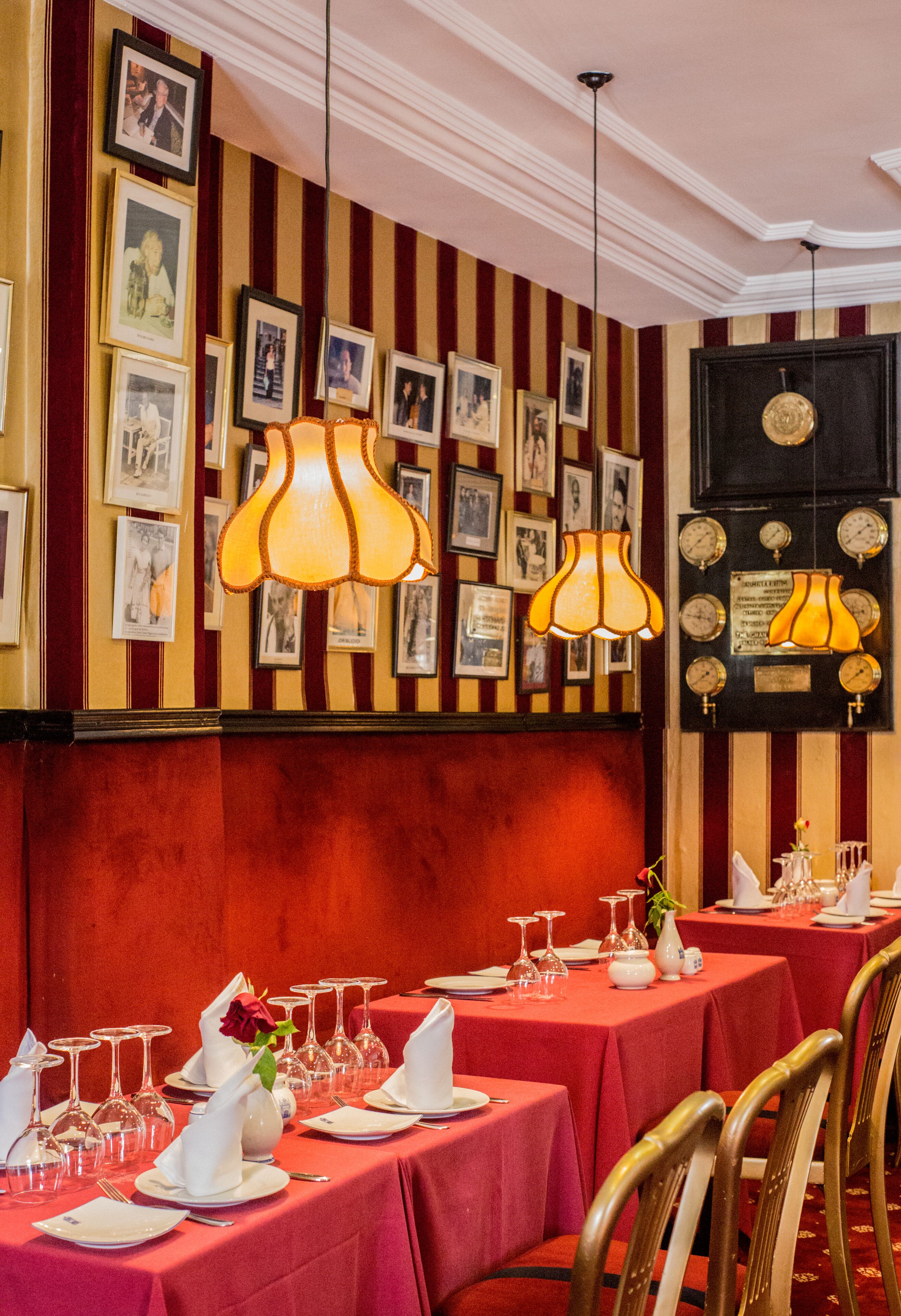 A dining area with tables set for service, framed pictures on the wall, and a vintage wall clock.