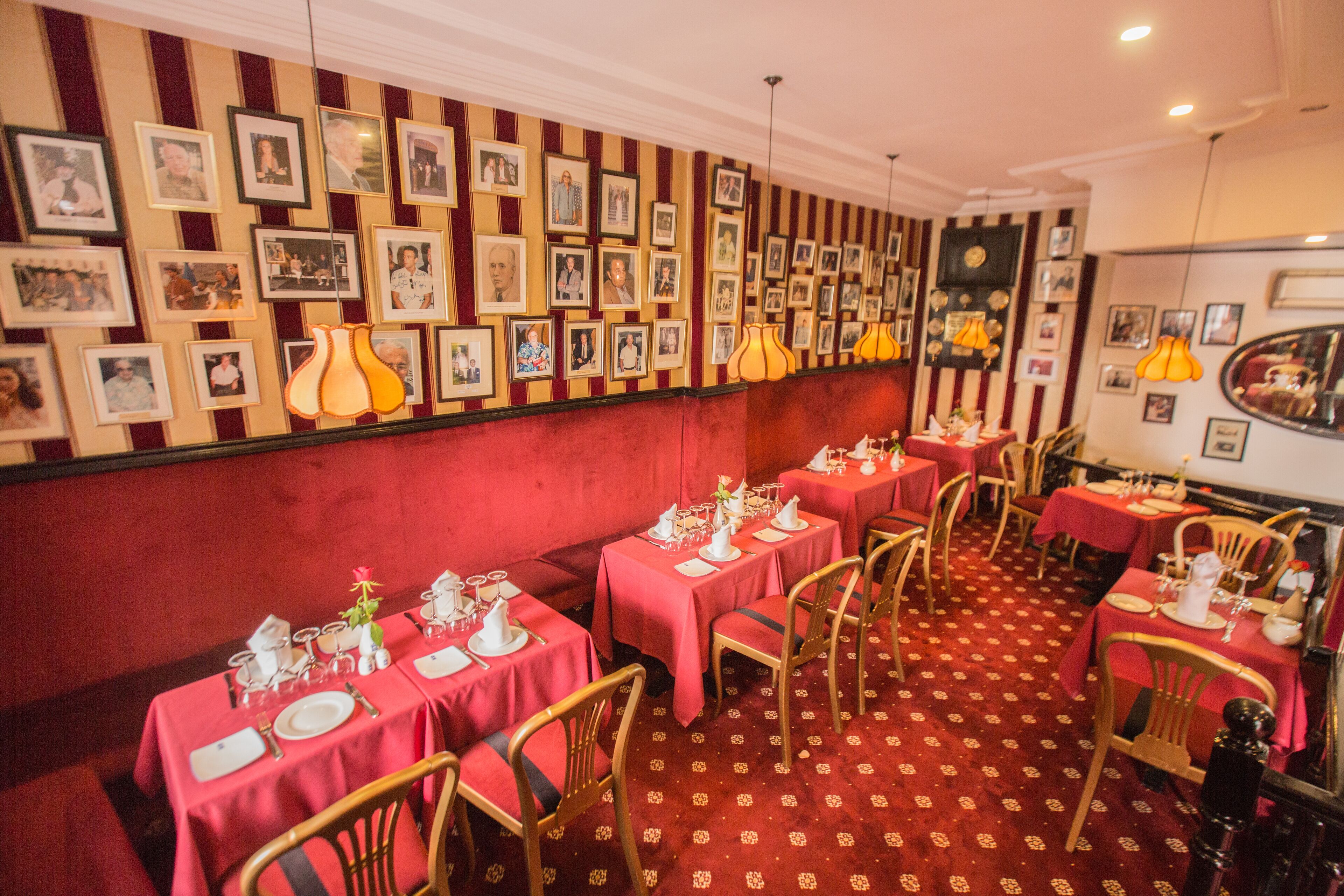 A restaurant with red and gold striped walls, multiple tables with white tablecloths, and framed pictures on the walls.