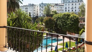 Un balcón con vista a una piscina, palmeras y un edificio al fondo.