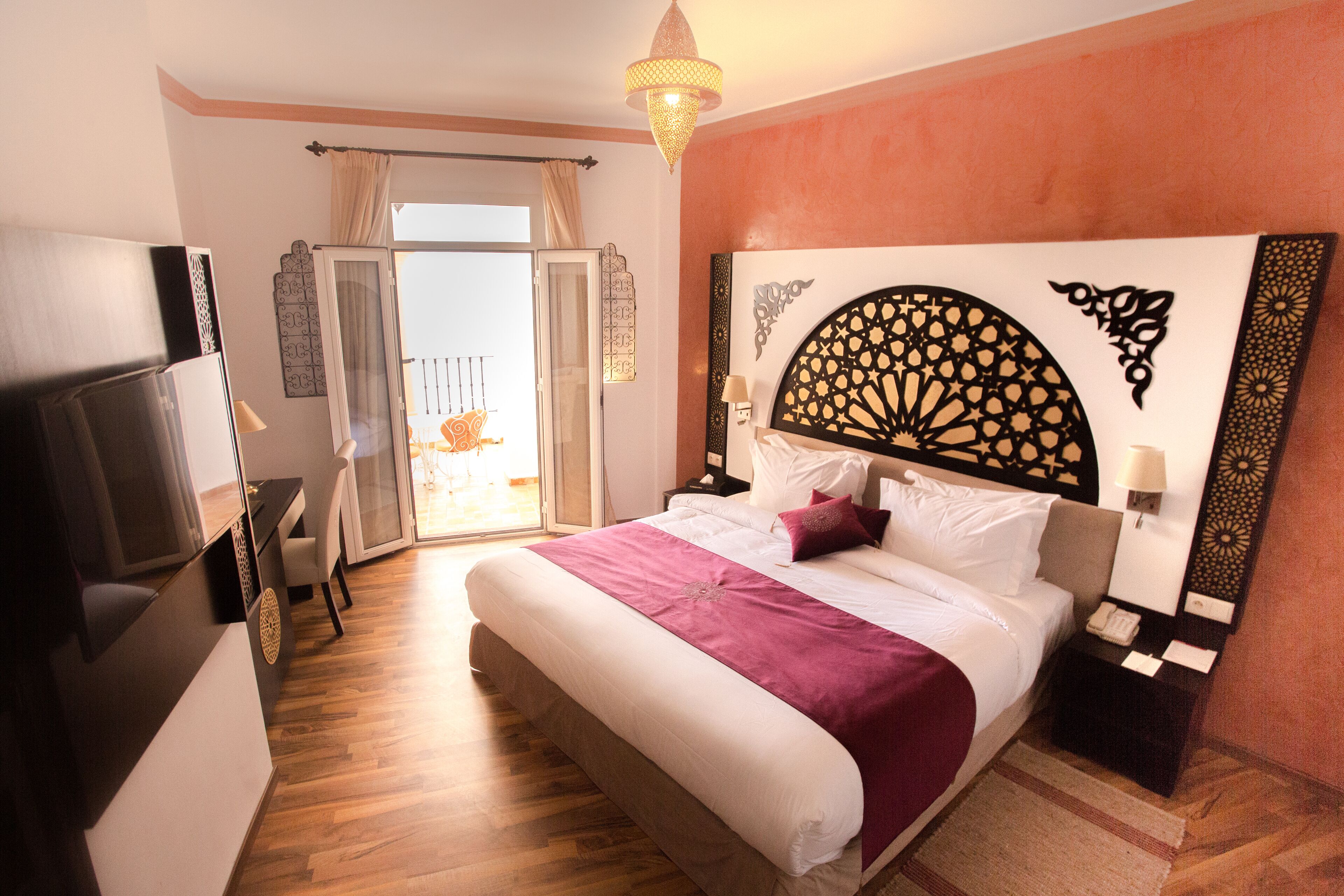 Una habitación de hotel con una cama grande, televisión, balcón y un cabecero decorativo.