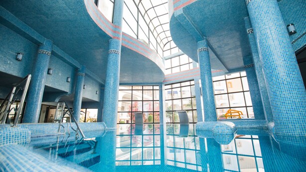 Una piscina interior moderna con mosaicos azules, ventanas amplias y techo curvo.