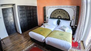 A double bed with a decorative headboard, two bedside tables, a red patterned rug, and a wooden floor.