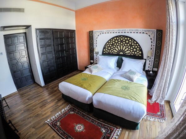 A double bed with a decorative headboard, two bedside tables, a red patterned rug, and a wooden floor.