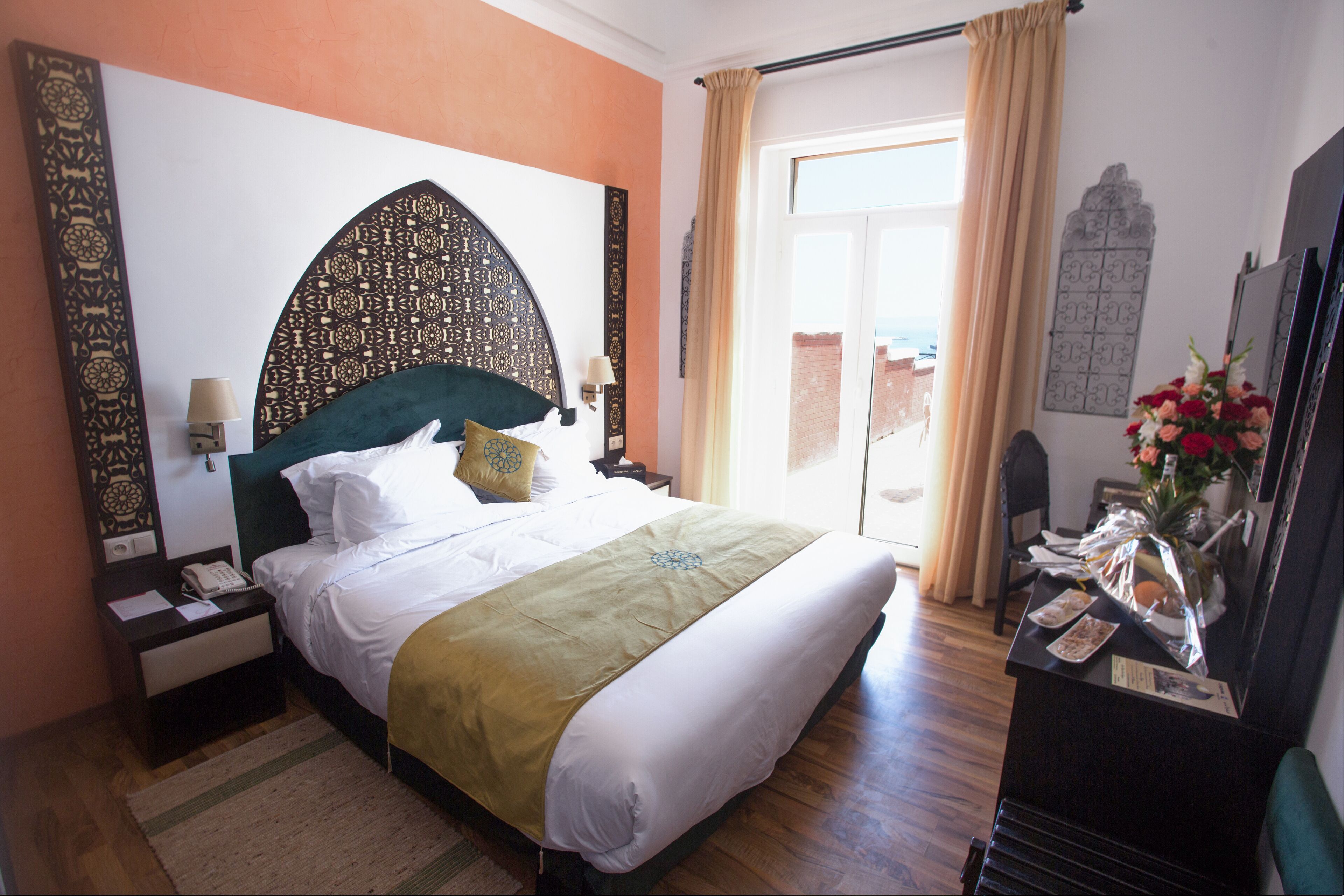 Habitación de hotel con una cama grande, una mesita de noche con teléfono, un escritorio con un florero y vistas al exterior a través de una ventana.