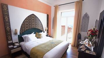 Habitación de hotel con una cama grande, una mesita de noche con teléfono, un escritorio con un florero y vistas al exterior a través de una ventana.
