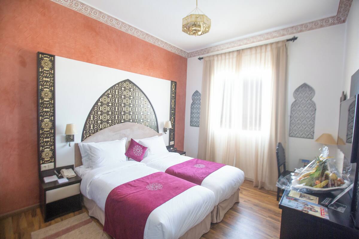 A hotel room with a large bed, two bedside tables, a TV, and a window with curtains.