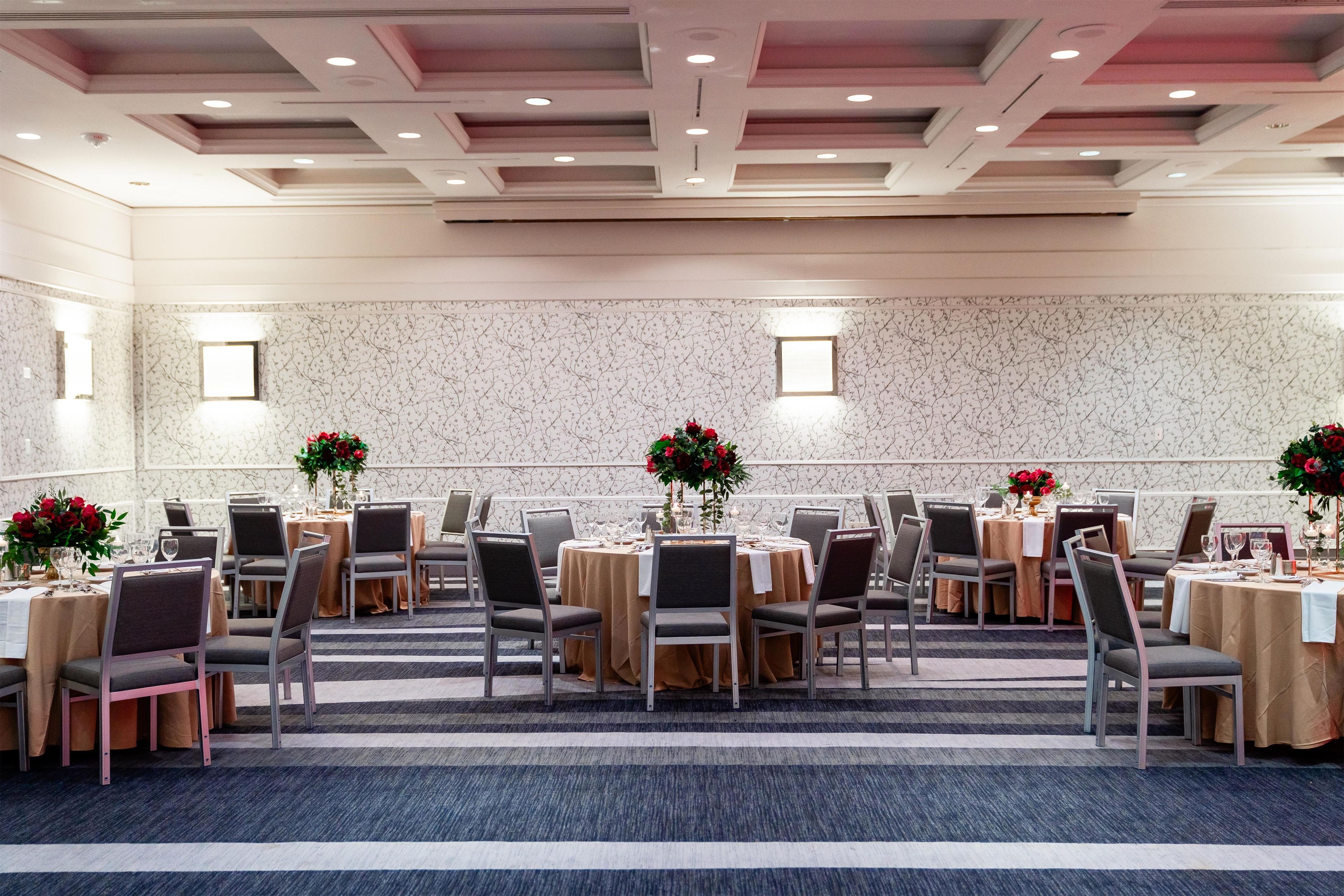 Un salón de conferencias con mesas redondas, sillas y centros de mesa con flores.