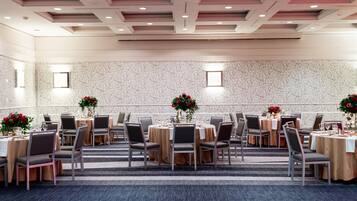 Un salón de conferencias con mesas redondas, sillas y centros de mesa con flores.