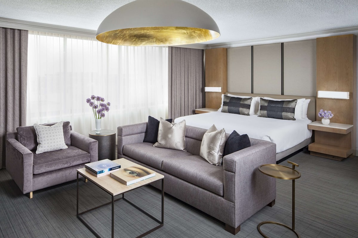 A modern hotel room with a large bed, a sofa, a coffee table, and a small side table.