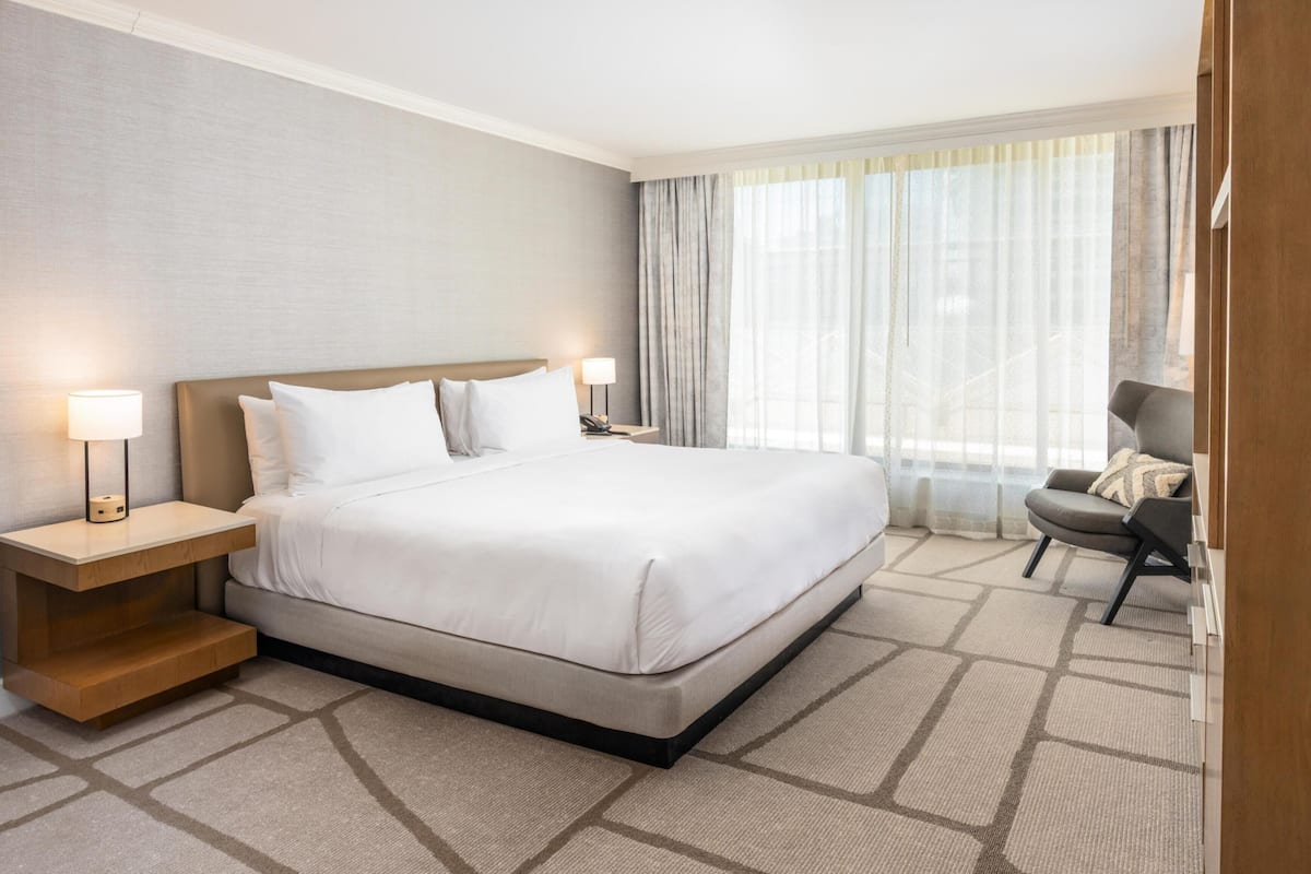 A hotel room with a bed, bedside lamps, a chair, and a window with curtains.
