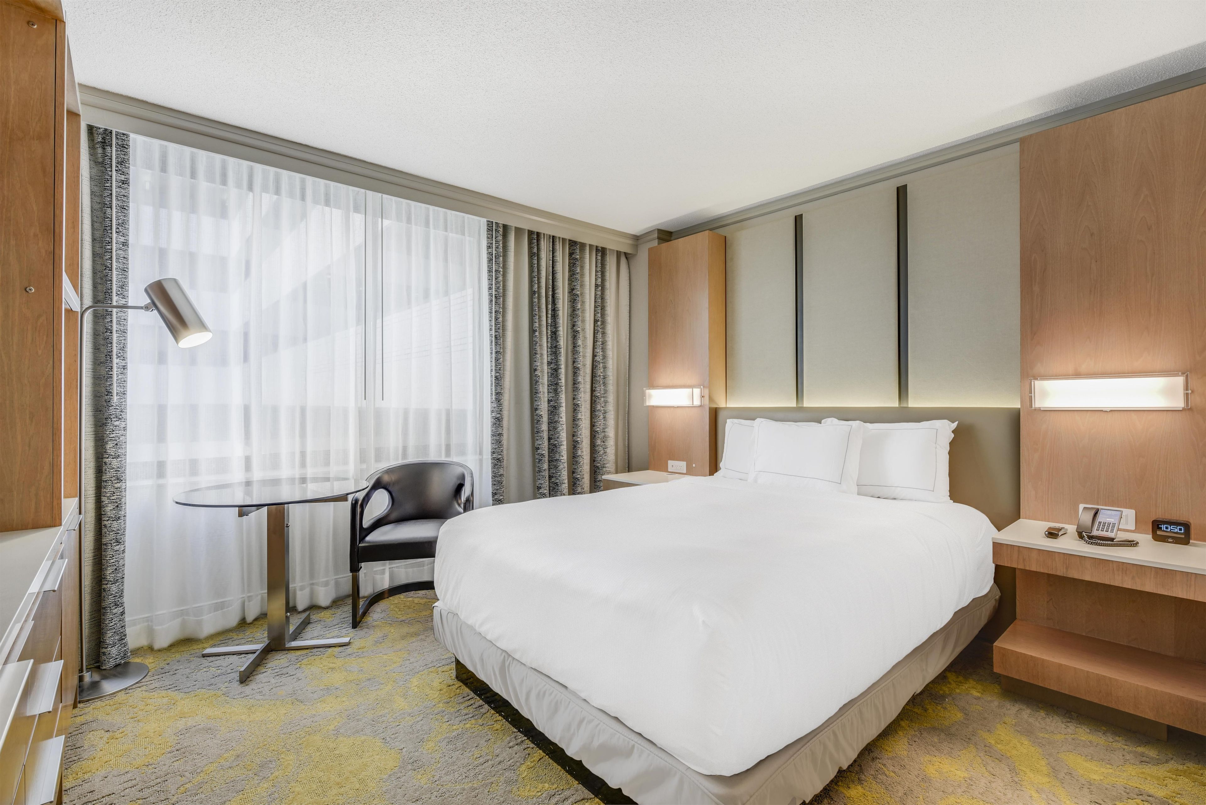 Une chambre d’hôtel avec un grand lit, un bureau, une chaise, une table de chevet avec une lampe et une horloge fixée au mur.