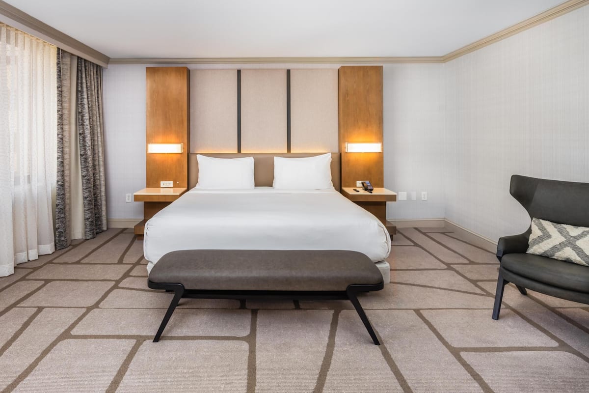 A hotel room with a large bed, bedside lamps, a chair, and a carpeted floor.