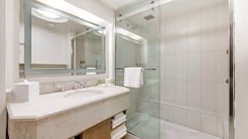 A modern bathroom with a marble sink, a large mirror, and a glass-enclosed shower.