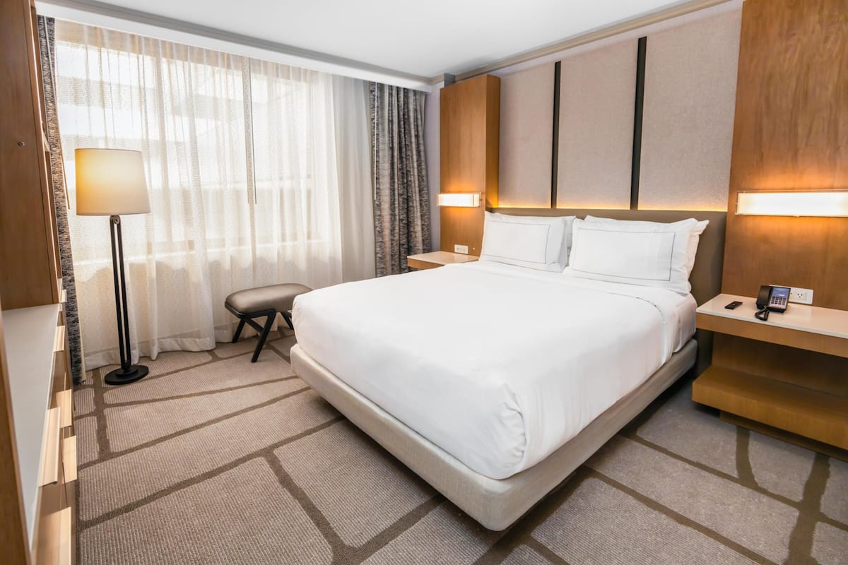 A hotel room with a large bed, a bedside table with a lamp, a chair, and a desk with a phone.