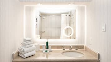 A bathroom with a large mirror, a sink, and a towel stack.
