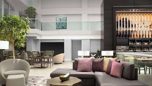 A modern hotel lobby with a sectional sofa, armchairs, a coffee table, and a bar area with bottles.