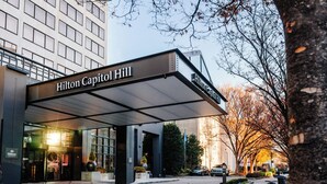 The exterior of the Hilton Capitol Hill hotel with a covered entrance, a Christmas tree, and a parking area with a scooter.