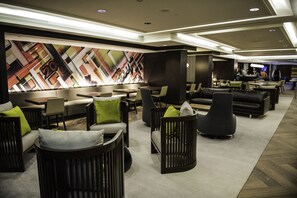 A modern hotel lobby with a geometric wall mural, multiple seating areas with sofas and chairs, and a bar area in the background. - Hilton Washington DC Capitol Hill (Washington)