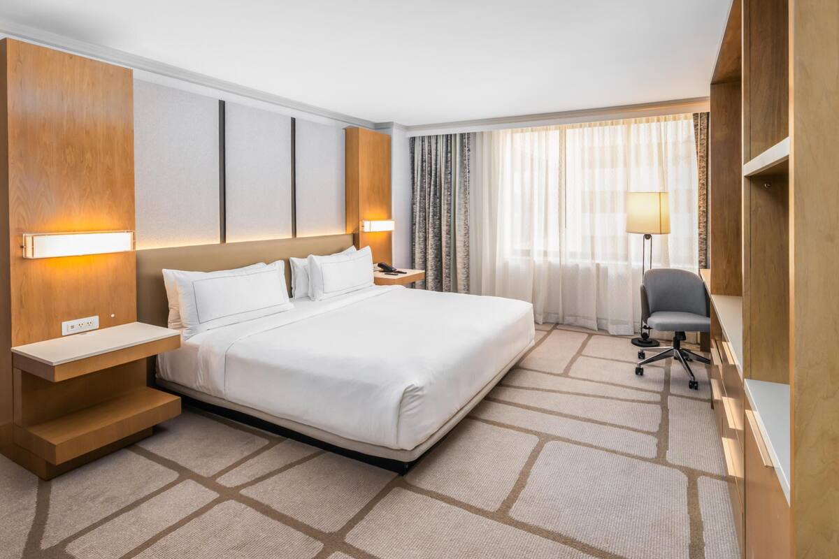 A hotel room with a large bed, bedside tables, a desk, and a chair.