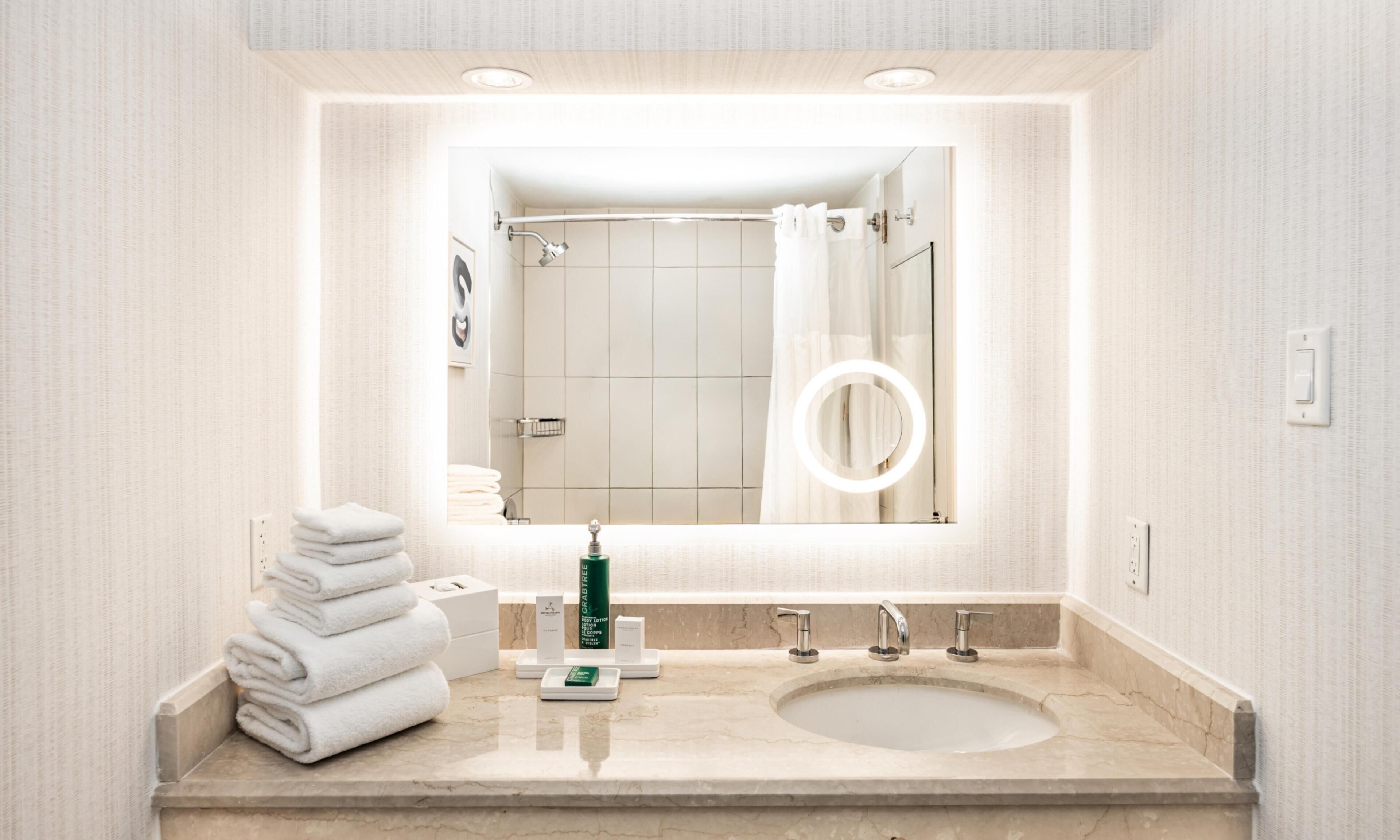 A bathroom with a large mirror, a sink, and a towel stack.
