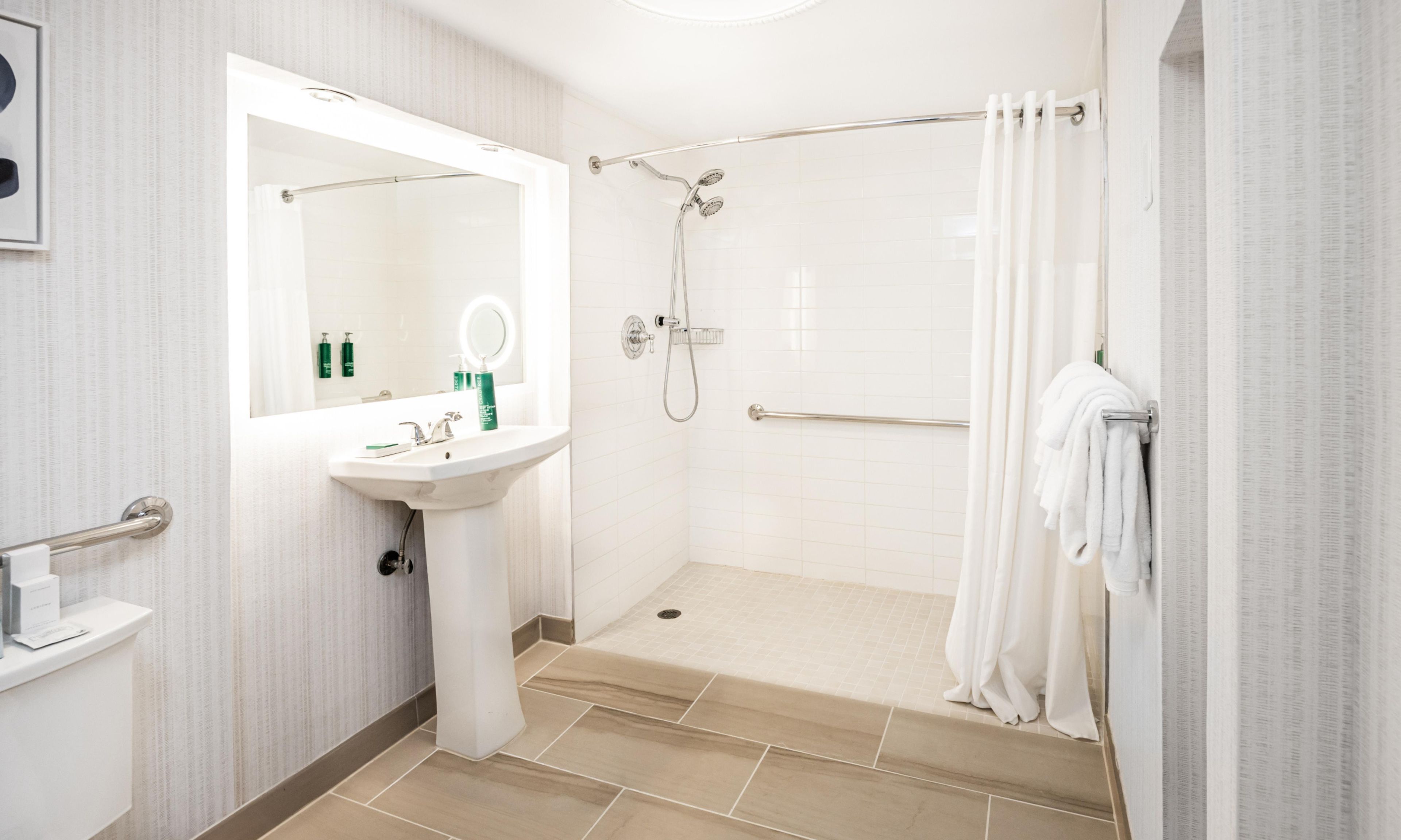 Un baño moderno con lavamanos, espejo, ducha y un perchero para toallas.