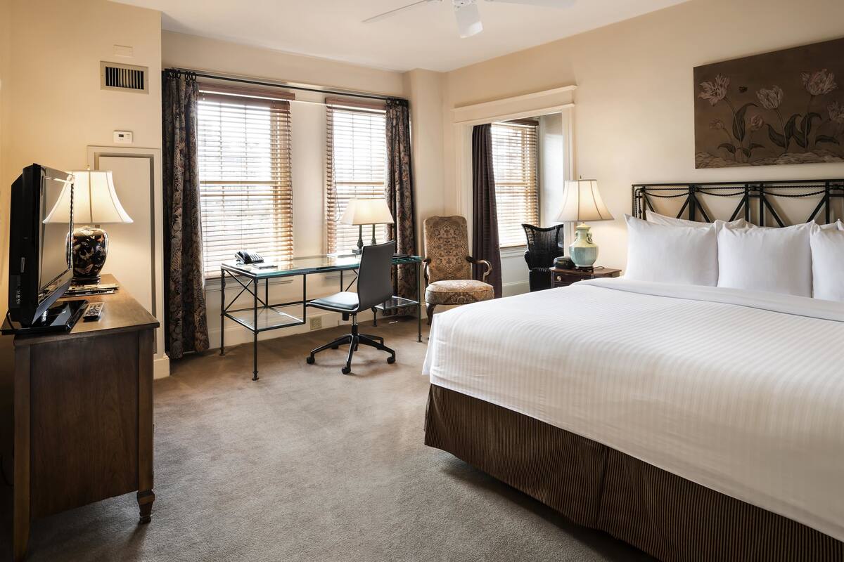 A hotel room with a large bed, a desk with a chair, a television, and a ceiling fan.