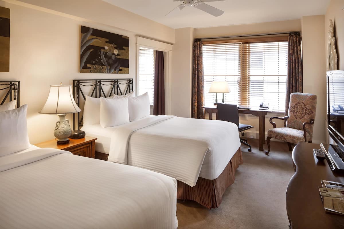 A hotel room with two beds, a desk, a chair, and a television.