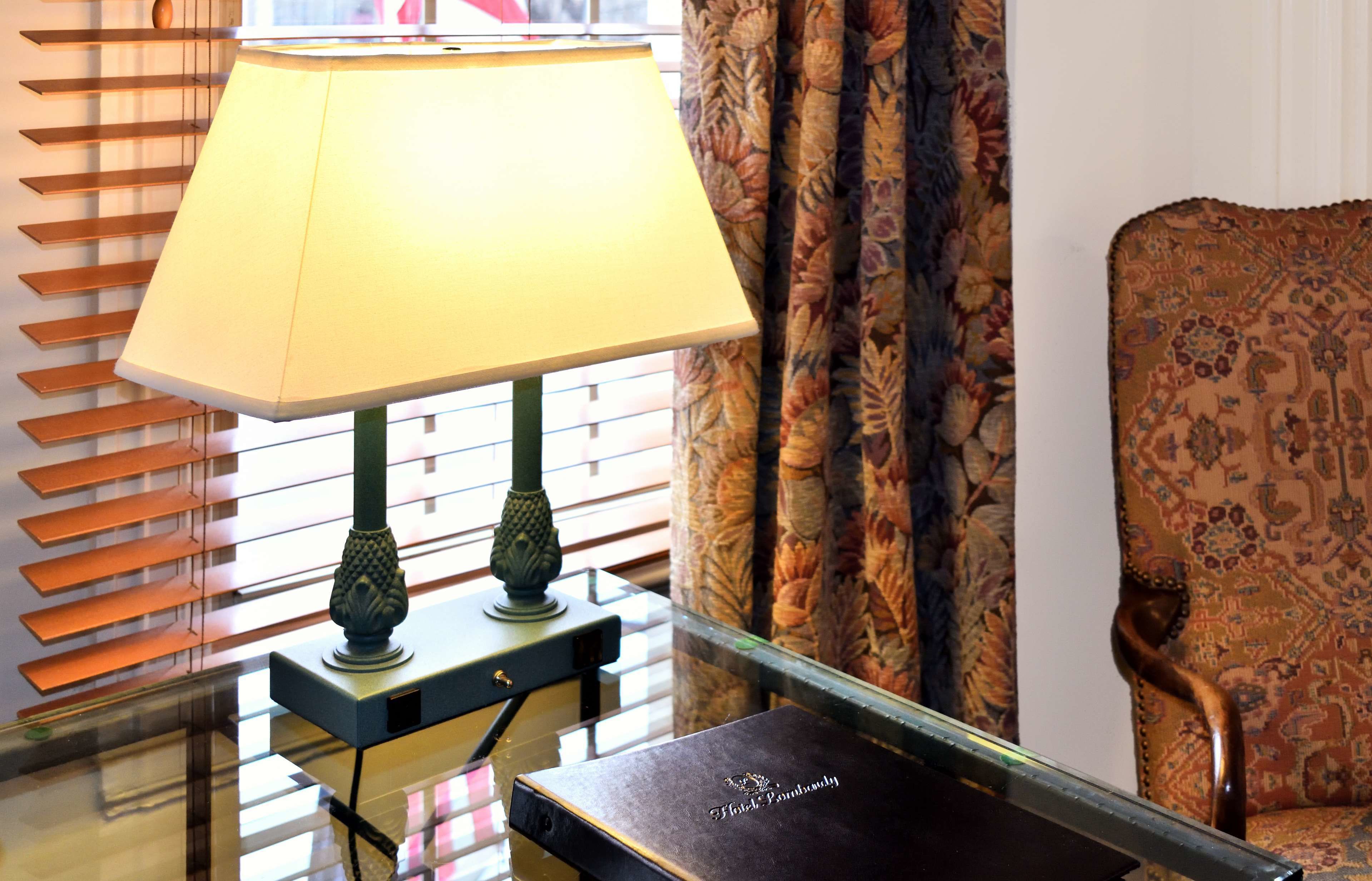 A room with a lamp on a table, a patterned chair, and a window with blinds.