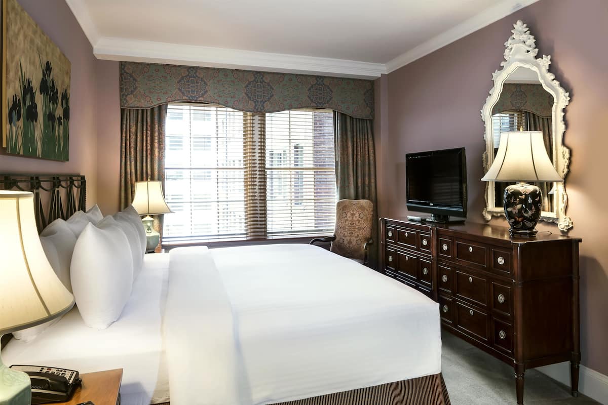 A hotel room with a large bed, a television, a dresser, and a mirror.
