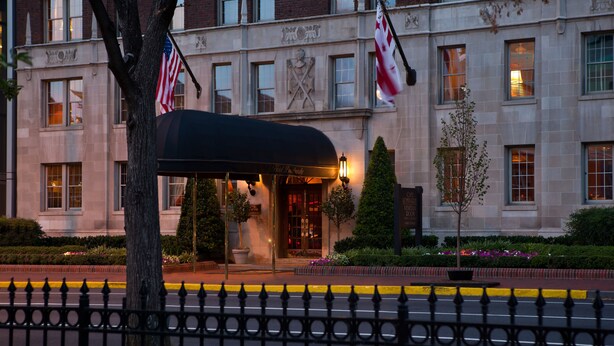Ein Hotel mit Eingangsbereich und überdachter Wartezone, amerikanischen Flaggen und einem gepflegten Garten.