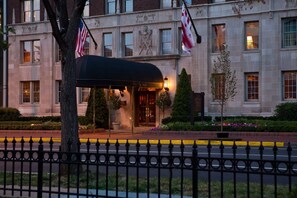 A hotel entrance with a covered waiting area, American flags, and a well-maintained garden. - Hotel Lombardy (Washington)