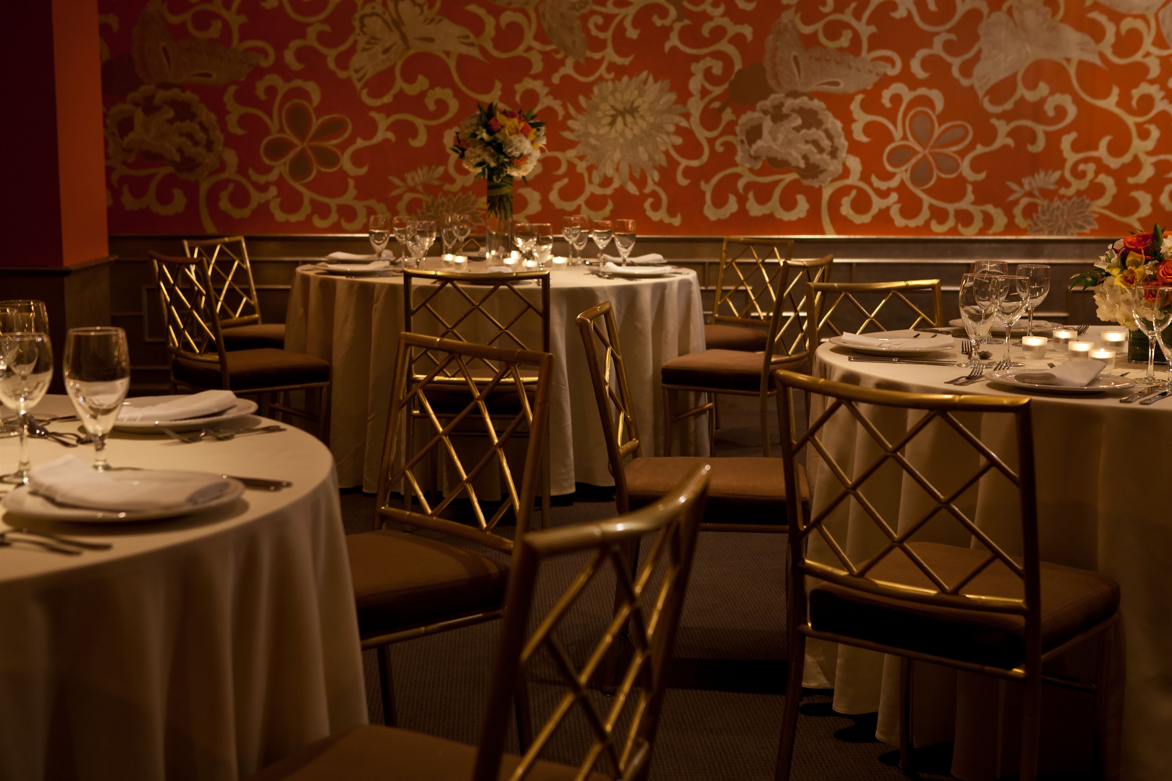 En restaurang med runda bord, gyllene stolar och blomsterarrangemang som mittpunkter.