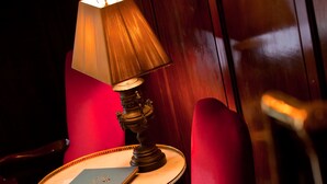Ein roter Sitzsessel, ein runder Holztisch mit einem Buch und einer Lampe, sowie ein gefliester Boden.