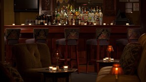 Eine Bar mit mehreren Stühlen, einer Theke voller Flaschen und Tischen mit Kerzen.