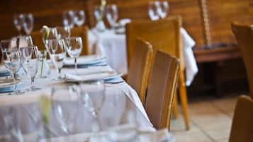 A dining table set with wine glasses, plates, and cutlery in a restaurant with wooden chairs and a white tablecloth.