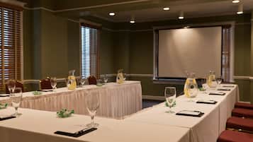 A conference room with a long table set for a meeting, equipped with chairs, a projector screen, and glassware.