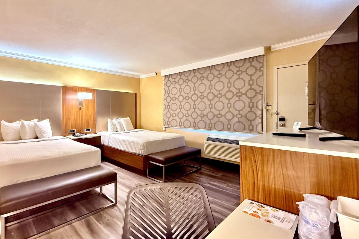 Ein Hotelzimmer mit zwei Betten, einem Schreibtisch, einem Stuhl, einer Bank, einem großen Spiegel und einer Wand mit Muster.