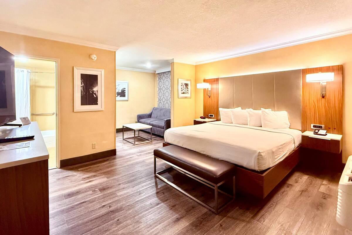 Ein Hotelzimmer mit Bett, Nachttisch, Lampe und Schreibtisch mit Fernseher.