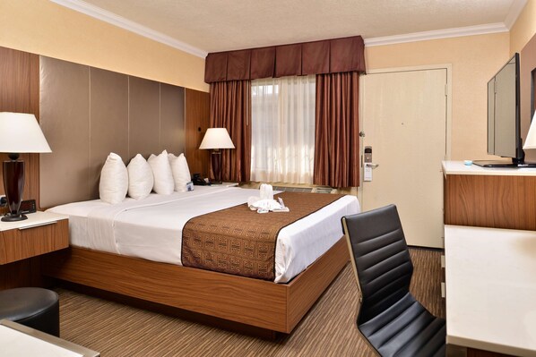 A hotel room with a wooden bed, two bedside lamps, a desk, a chair, and a television.