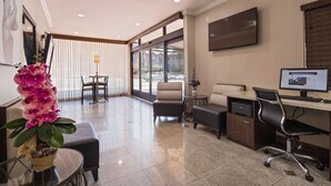A modern hotel lobby with a seating area, a desk with a computer, and a large window offering a view of the street. - Best Western Hollywood Plaza Hotel - Walk of Fame Film City LA (Los Angeles)