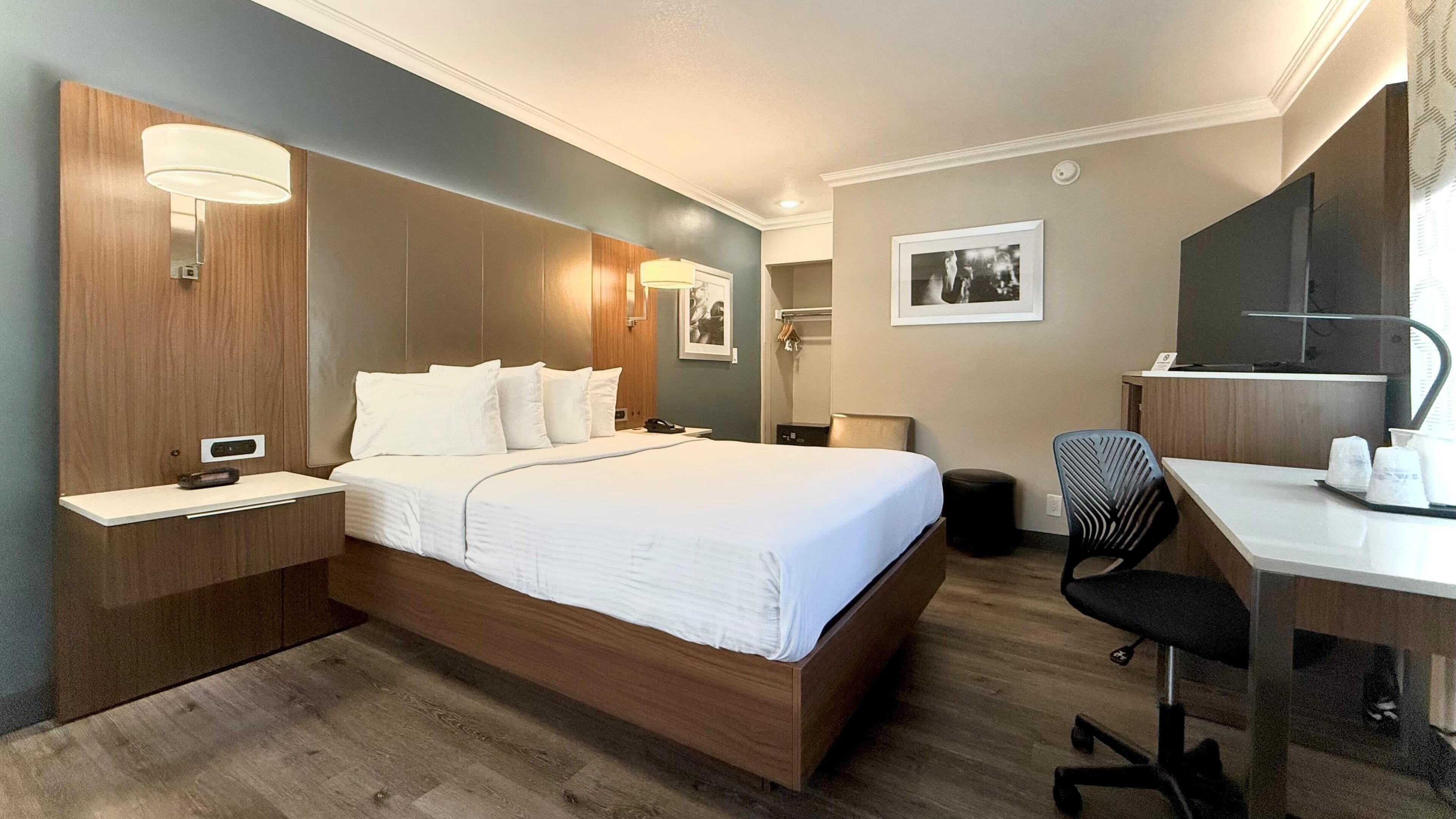 A hotel room with a bed, bedside table, desk, chair, and a mirror.